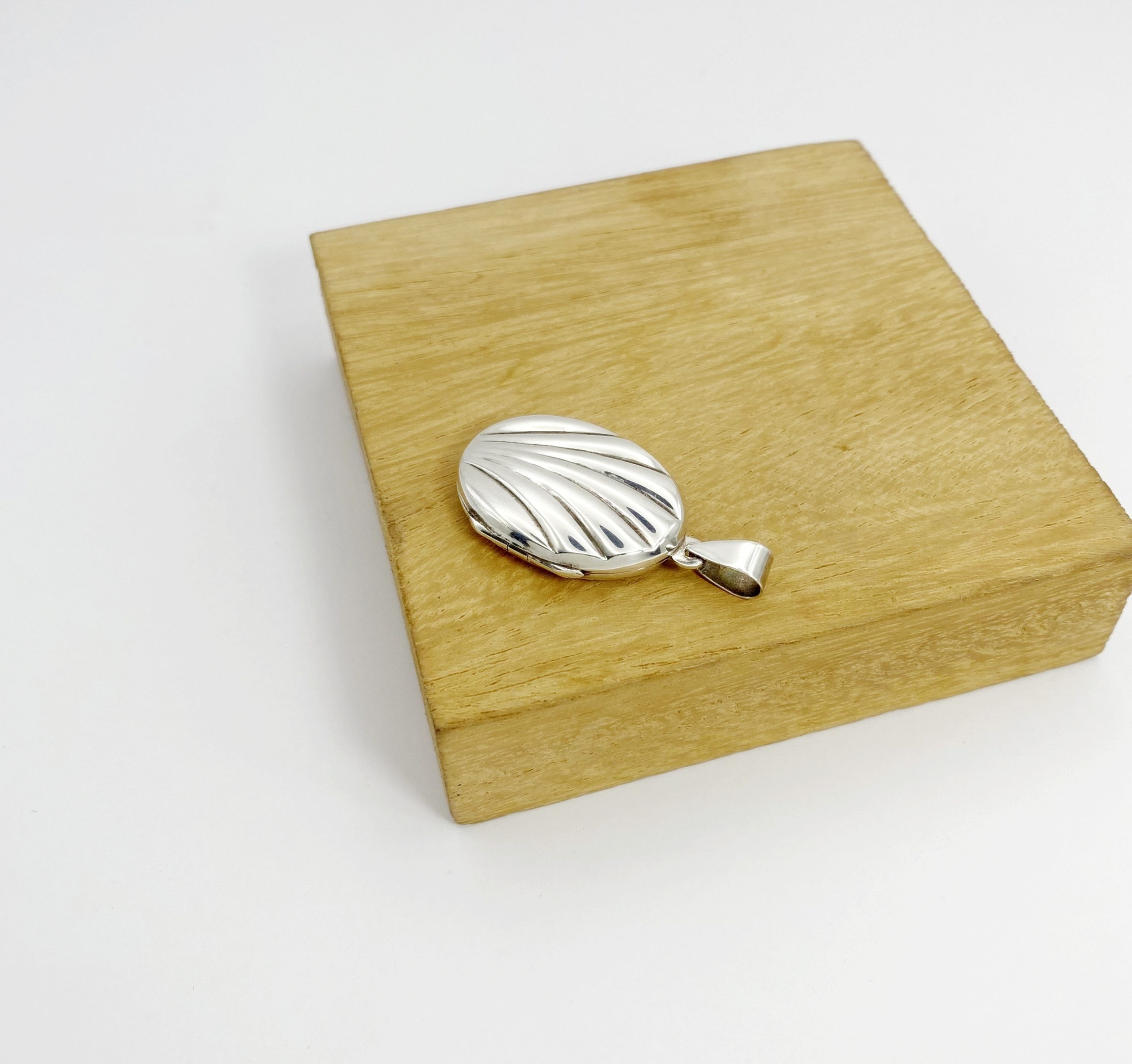 Side angle view of the front cover of a silver photo locket resting on a wooden block, highlighting the detailed hinge construction.