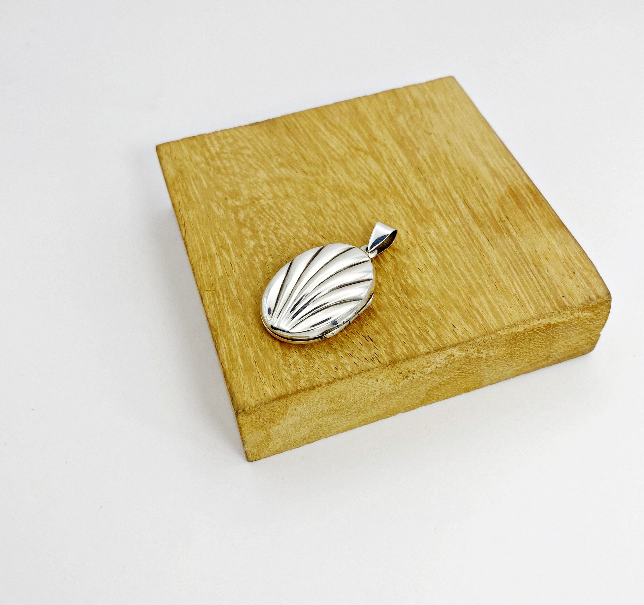Right side profile view of an oval 925 silver pendant locket displayed elegantly on a square wooden holder.