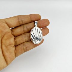 Hand holding a closed oxidized 925 sterling silver oval locket showcasing the detailed shell textured front design.