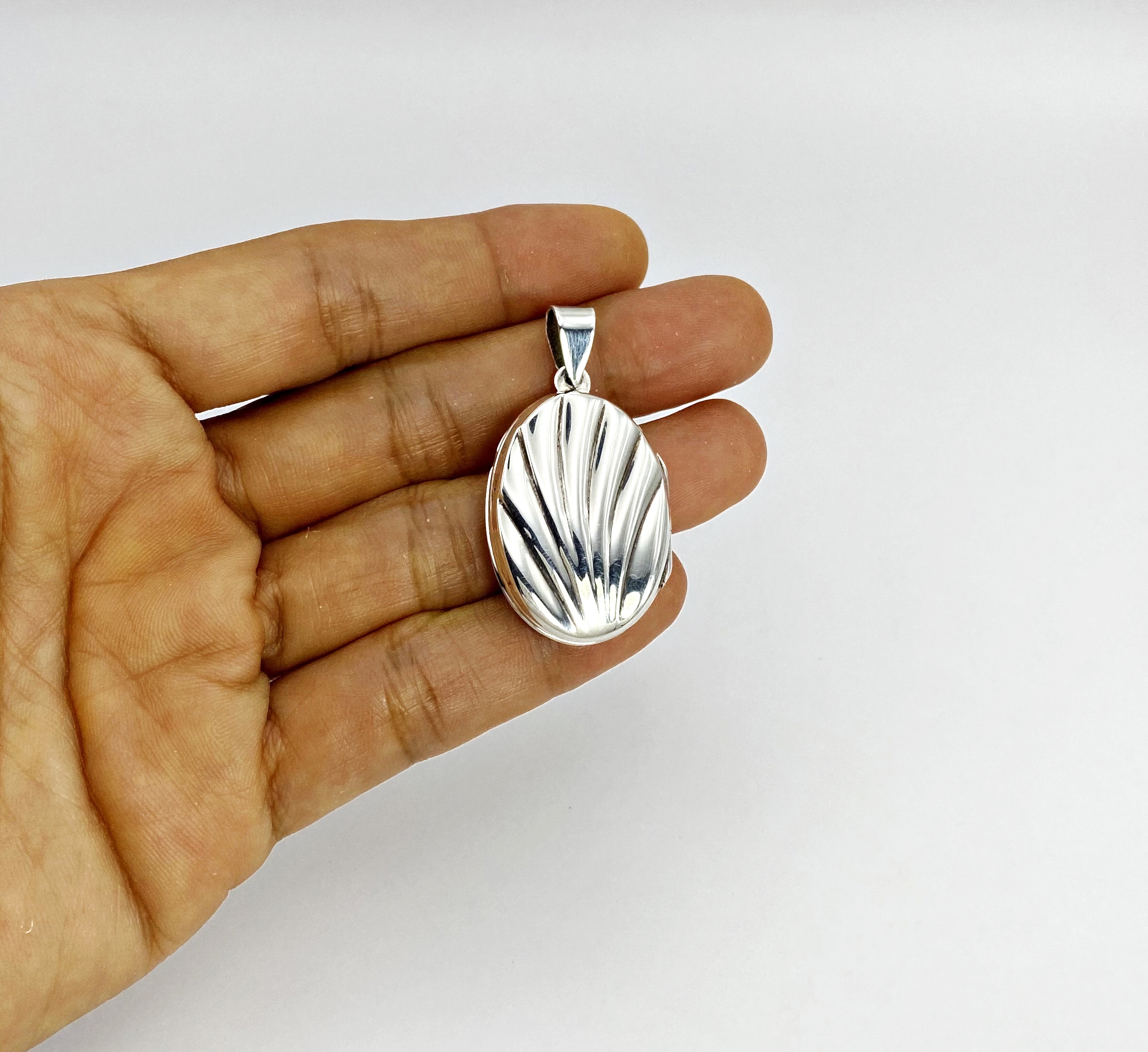 Hand holding a closed oxidized 925 sterling silver oval locket showcasing the detailed shell textured front design.