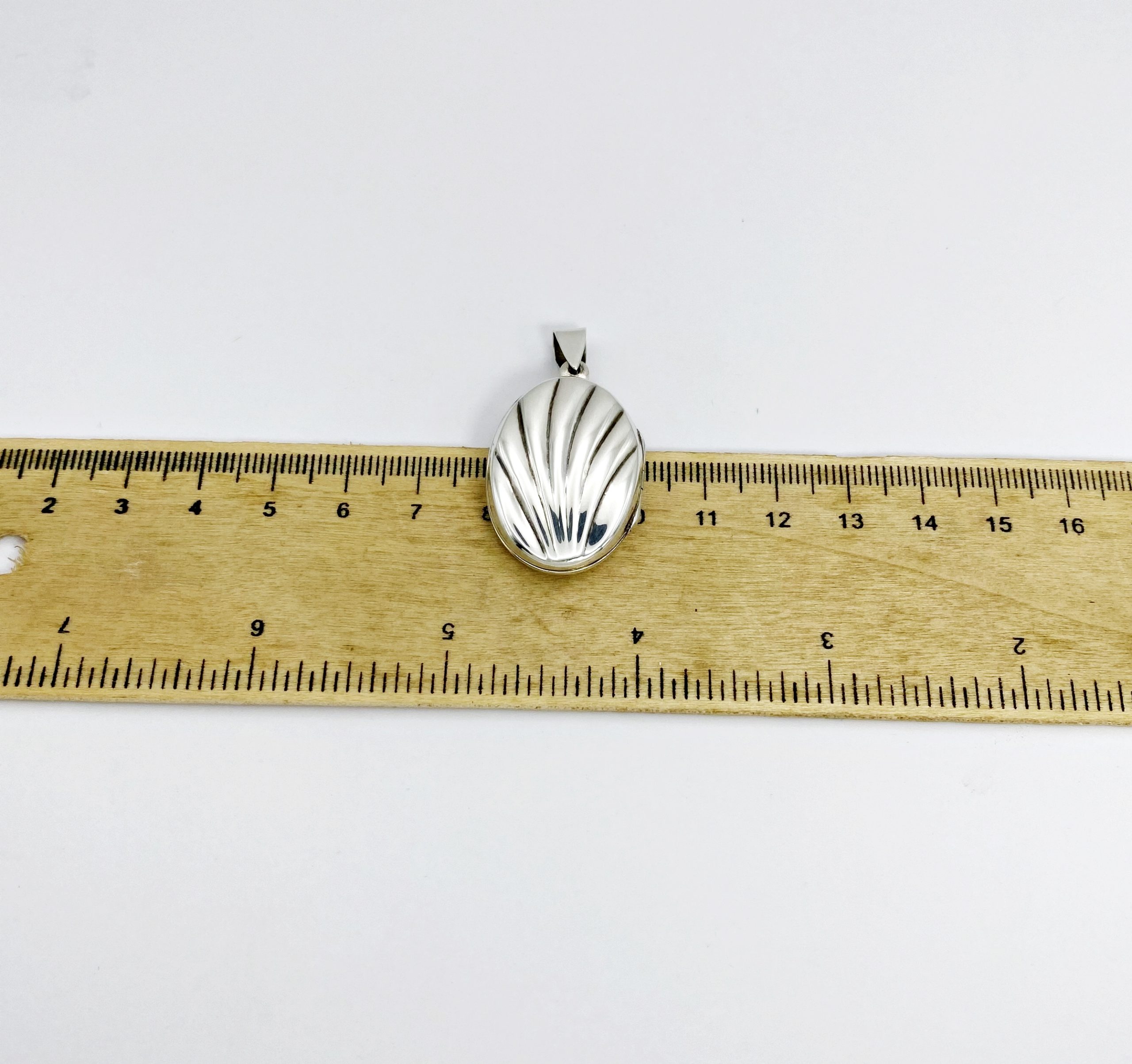 An oxidized silver shell locket placed next to a ruler measuring its width in centimeters for product scale.