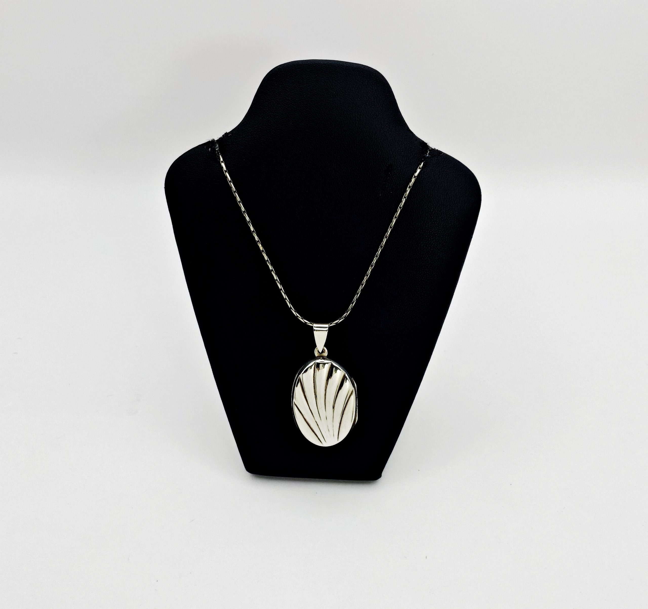 Oxidized sterling silver shell locket hanging on a delicate silver chain over a black velvet neck mannequin display.