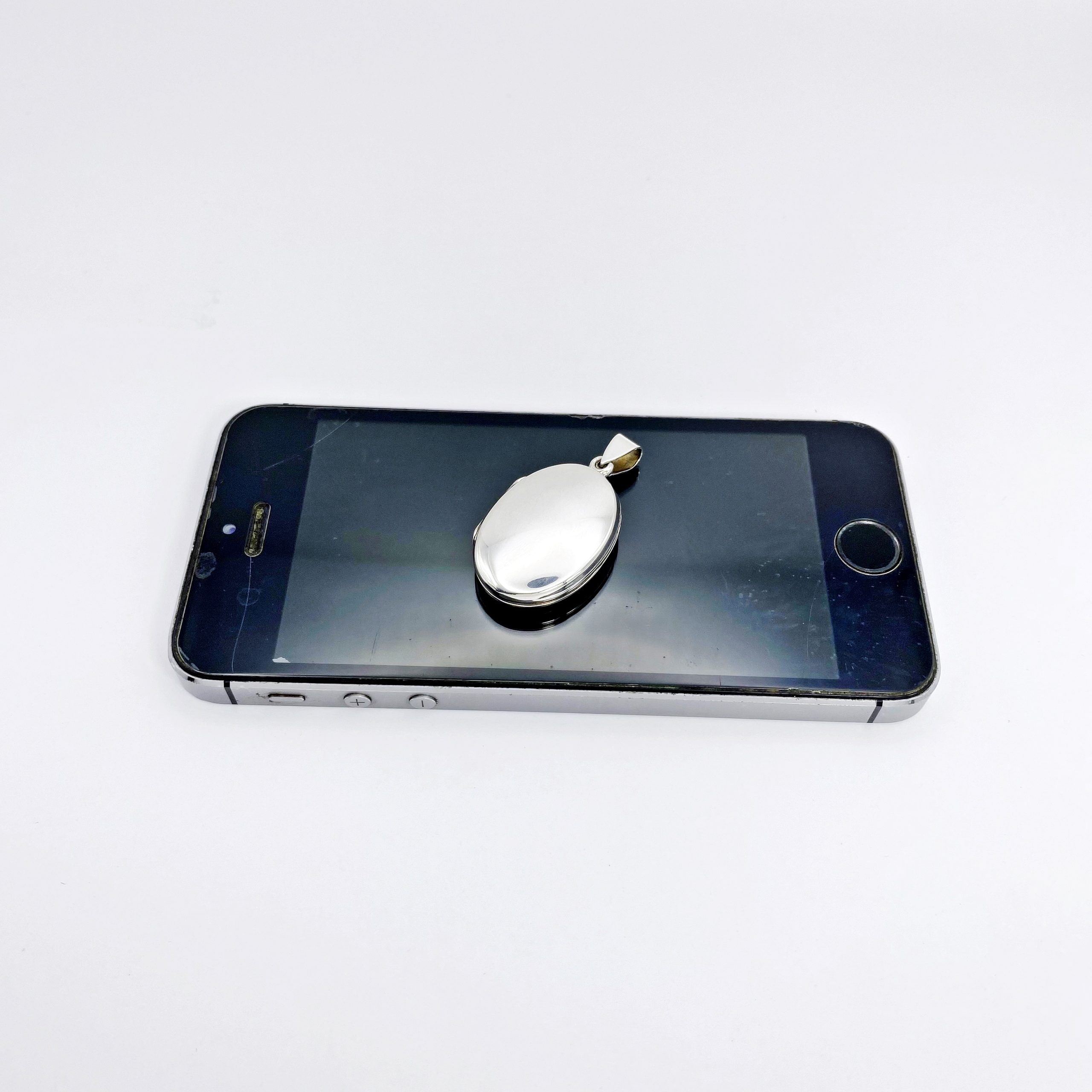 The sleek high-polish back of an oval sterling silver locket resting on a mobile phone screen display.