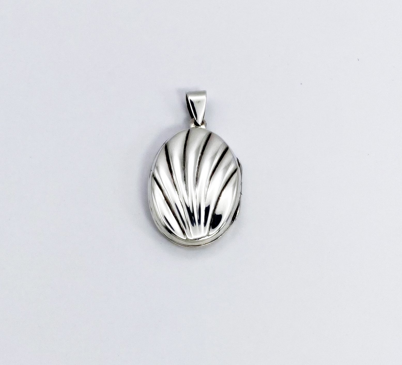 Studio product shot of the front cover of a shell-textured photo locket pendant in solid 925 sterling silver.