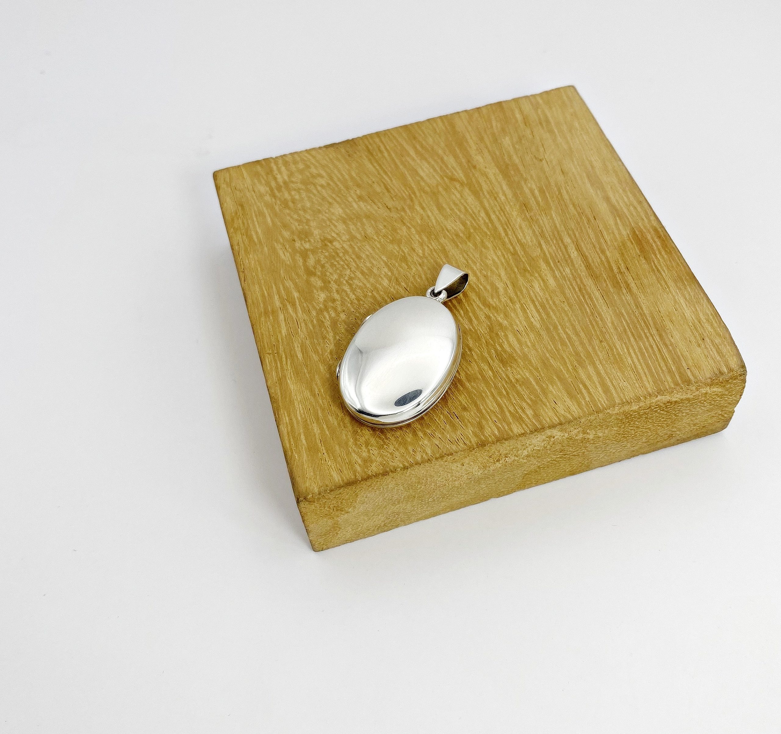 The smooth high-polish back of a sterling silver shell locket displayed flat on a square wooden block holder.