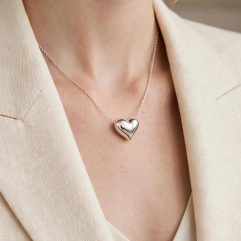 Close-up of a model wearing a shiny 925 sterling silver puffed heart slider necklace with a cream blazer.