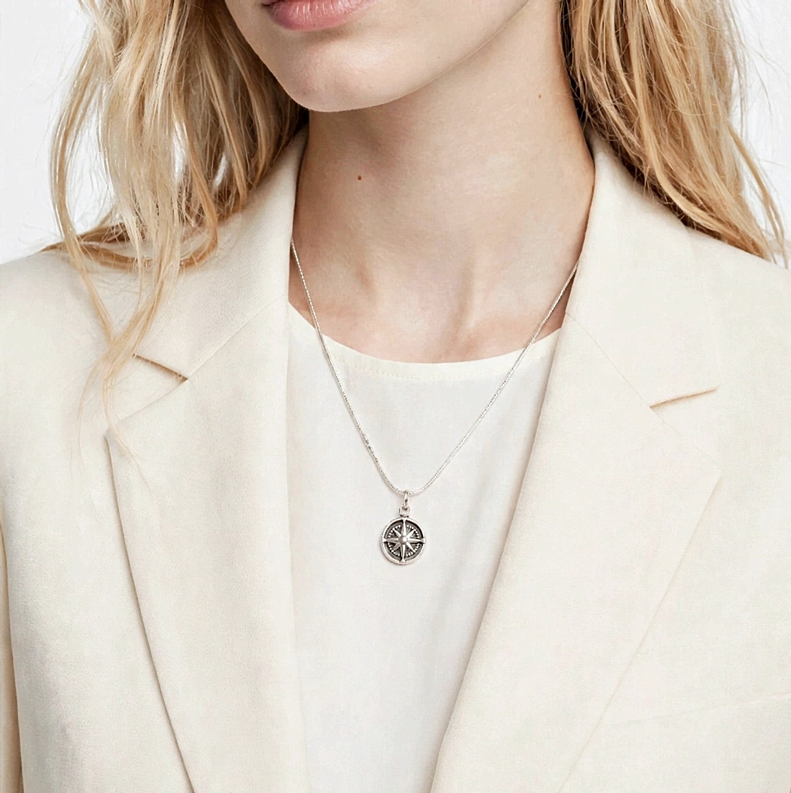 Close-up of model wearing the small oxidized sterling silver compass rose pendant over a cream blazer.
