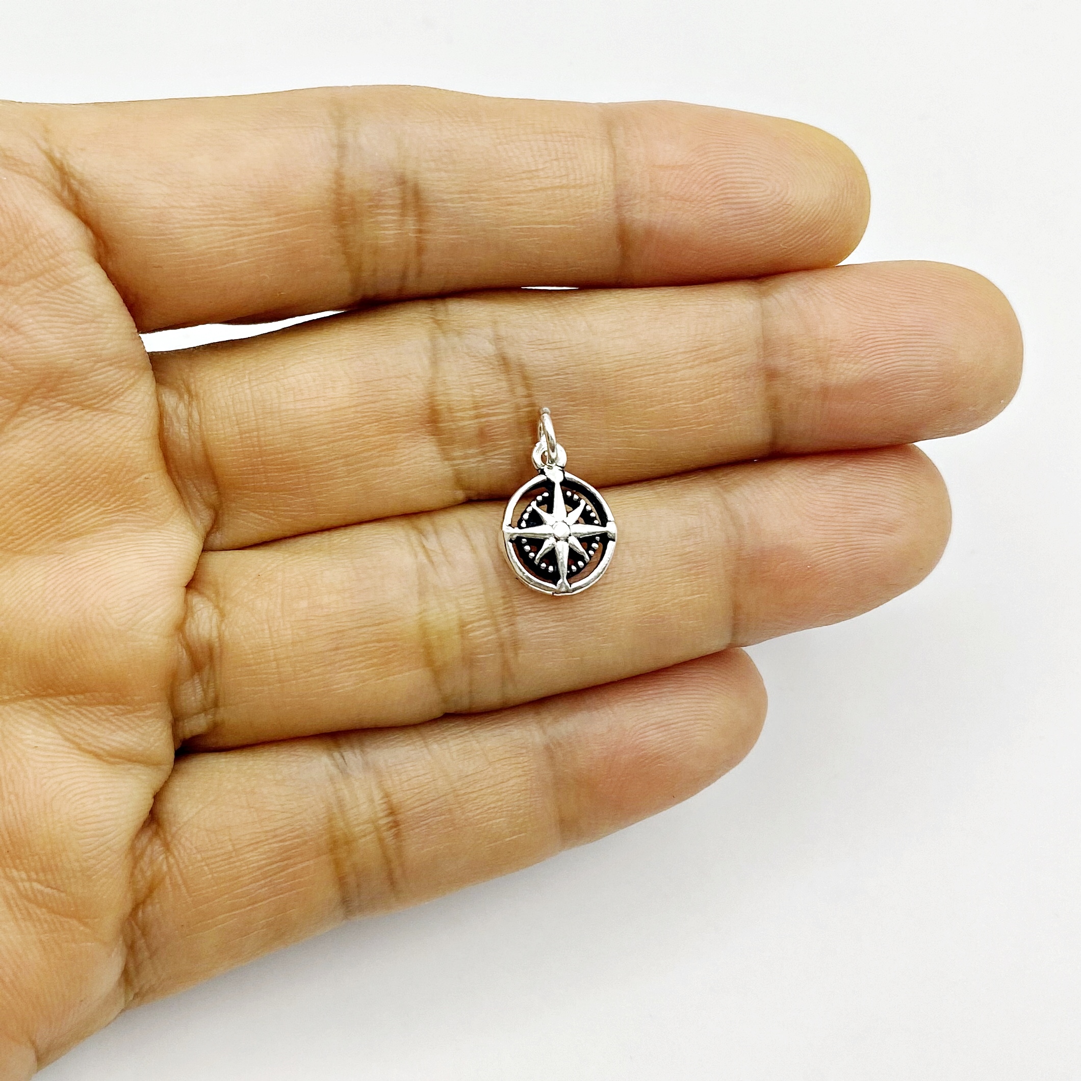 Hand holding the tiny 925 sterling silver compass rose pendant charm to show scale and double-sided detail.