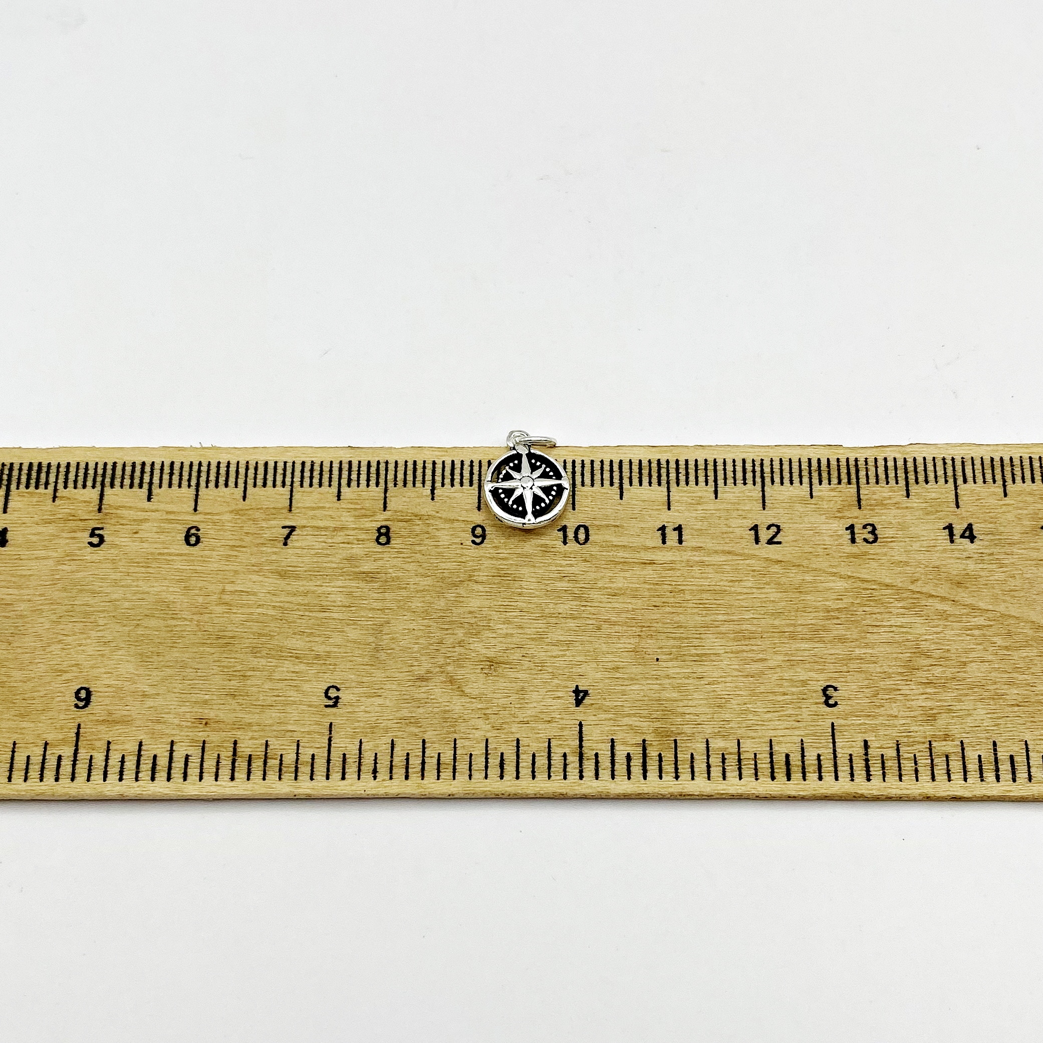 925 sterling silver compass rose pendant placed on a wooden ruler for precise size measurement.